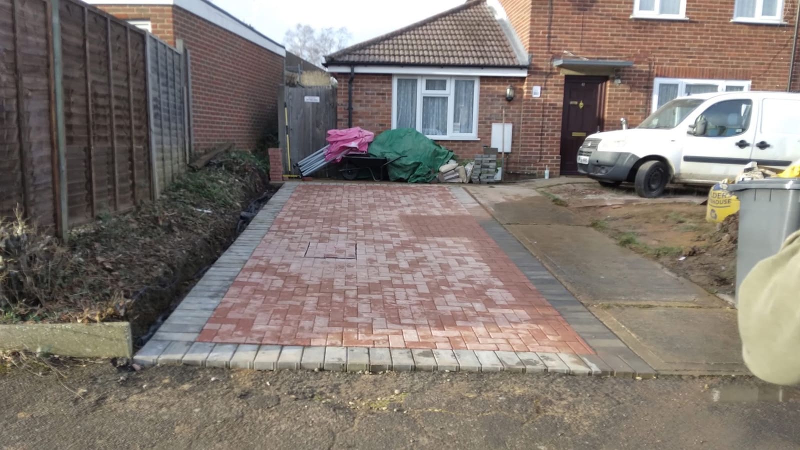 Completed red block paving driveway laid in stretcher bond with charcoal edging kerbs, running from the road up to a brick bungalow