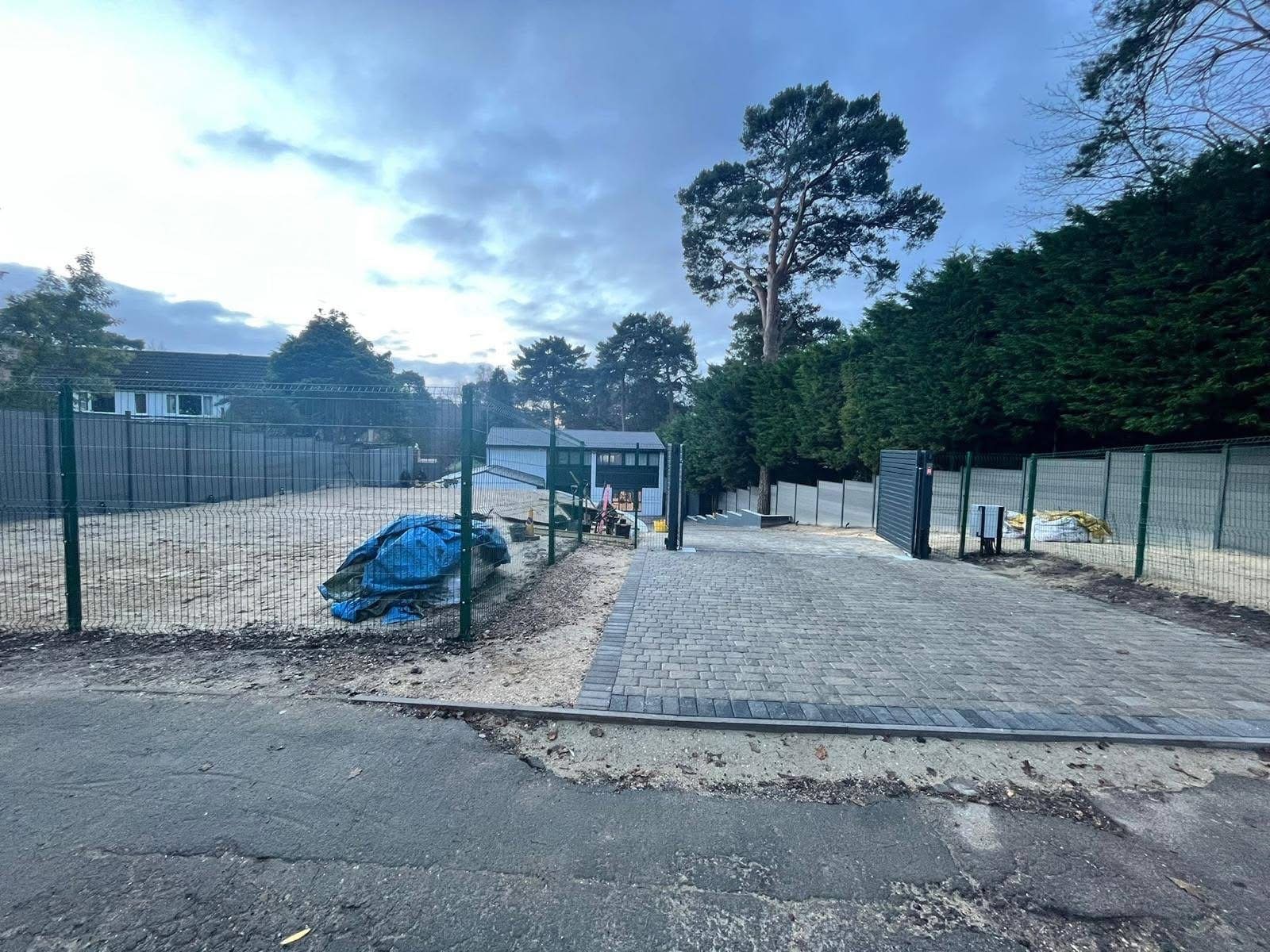 Green weldmesh security fencing and a grey aluminium entrance gate alongside a newly block-paved access driveway