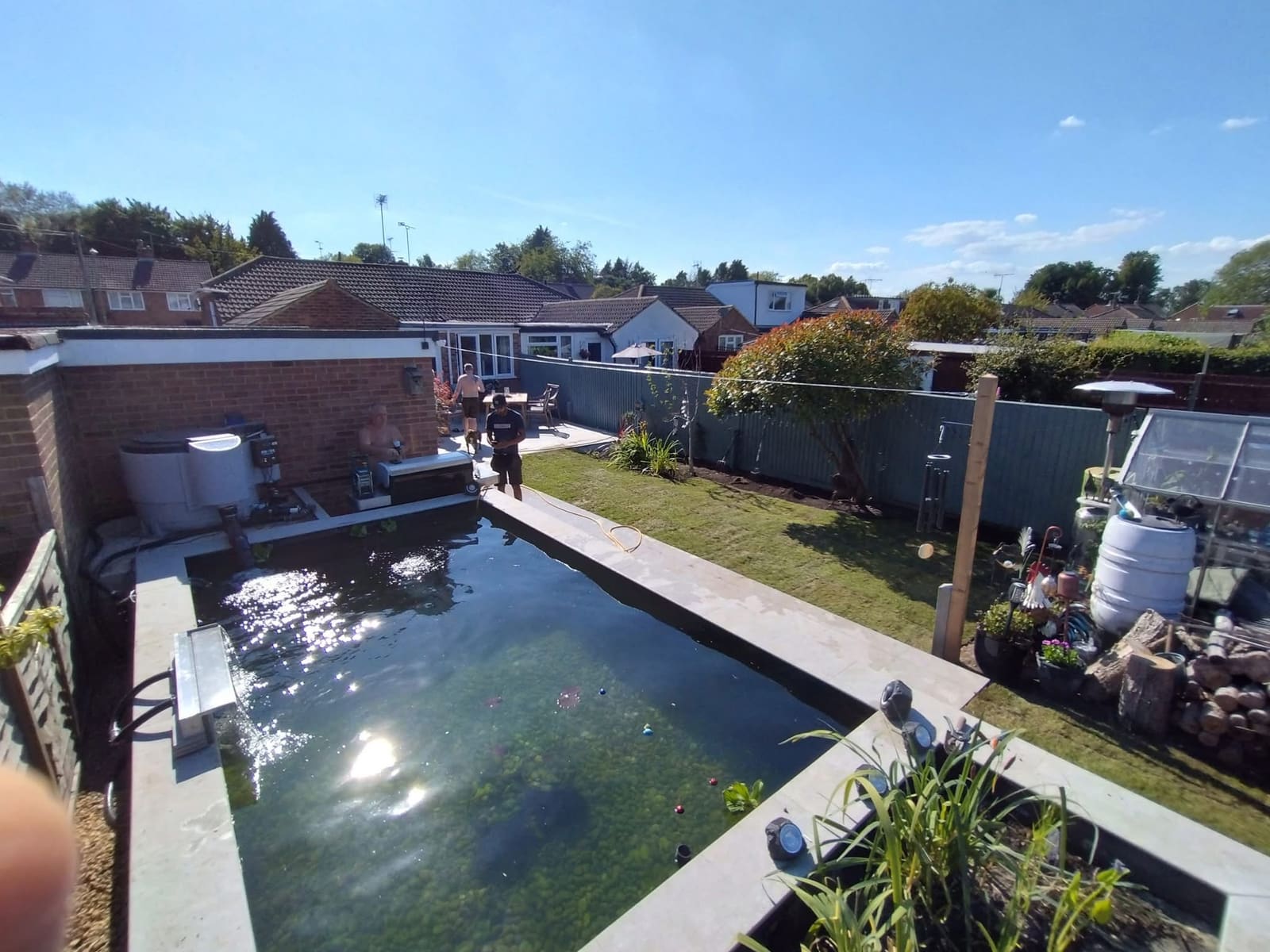 Raised rectangular formal pond with porcelain coping and paved margins in a rear garden, with pump and filtration housing built into the brickwork behind it
